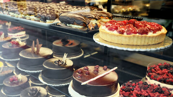 Showcase with a selection of cakes and pastries, including chocolate and berry cakes at the ATLANTIC Grand Hotel Travemünde.