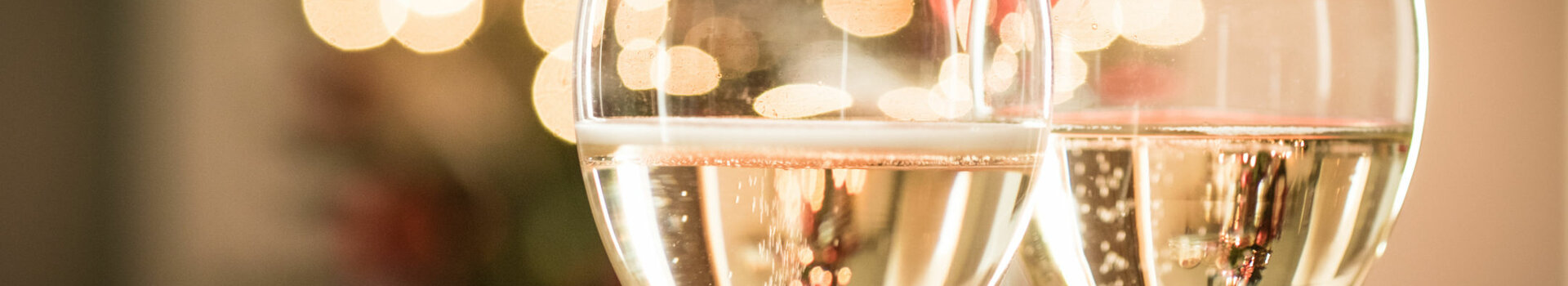 Zwei Sektgläser vor unscharfen, festlichen Lichtern.