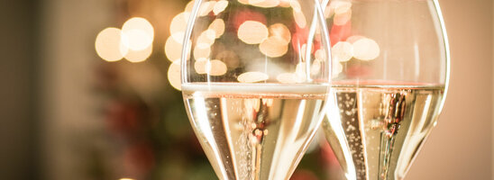 Zwei Sektgläser vor unscharfen, festlichen Lichtern.