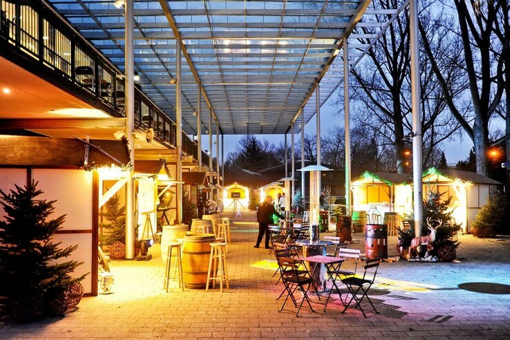 Überdachter Außenbereich mit Sitzgelegenheiten und beleuchteten Ständen im ATLANTIC Hotel Galopprennbahn.