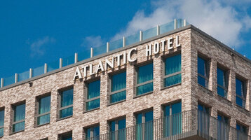 Fassade des ATLANTIC Hotel Kiel aus Backstein mit großen Fenstern und dem Hotelnamen in weißen Buchstaben.