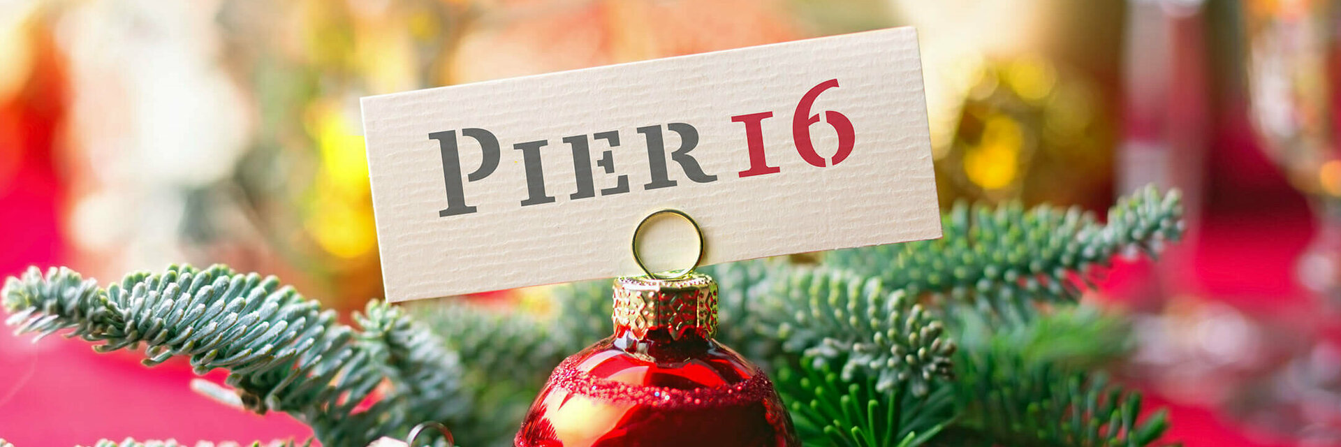 Weihnachtlicher Tannenzweig und Weihnachtskugel halten ein "PIER16" Schild