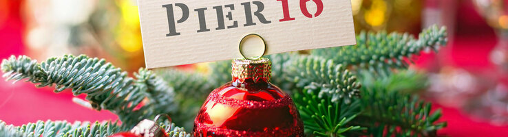 Weihnachtlicher Tannenzweig und Weihnachtskugel halten ein "PIER16" Schild