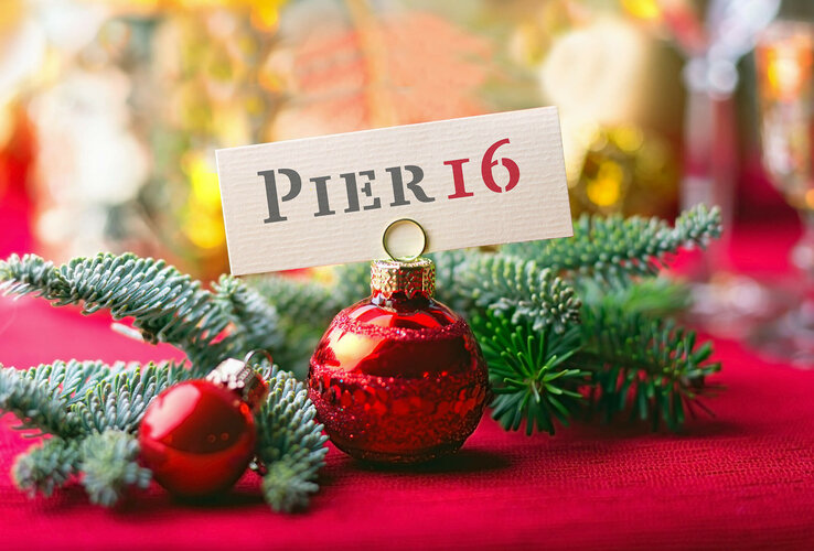 Weihnachtlicher Tannenzweig und Weihnachtskugel halten ein "PIER16" Schild