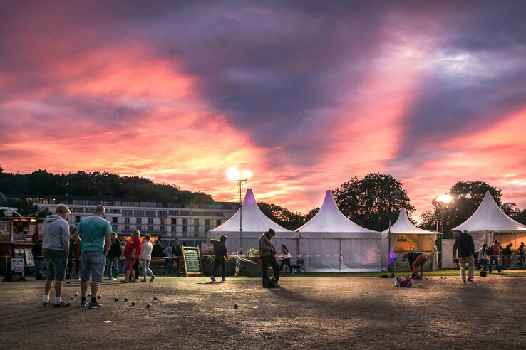 Menschen spielen Boule bei Sonnenuntergang vor weißen Zelten in Travemünde.