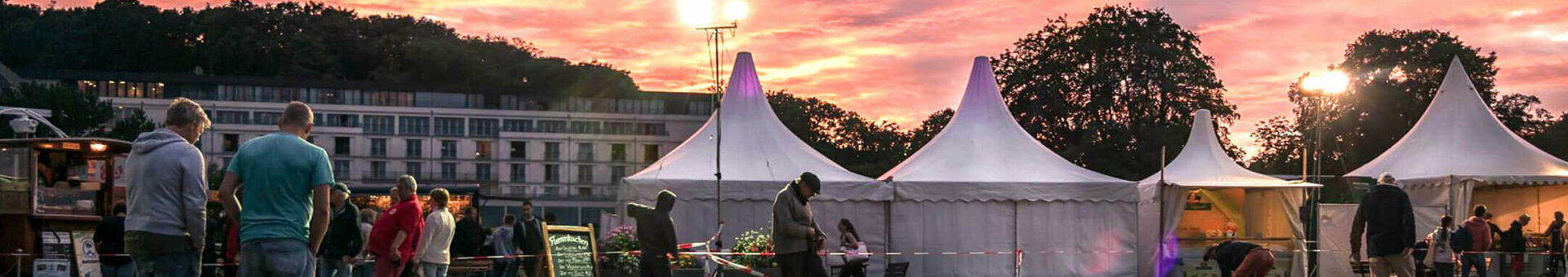 Menschen spielen Boule bei Sonnenuntergang vor weißen Zelten in Travemünde.