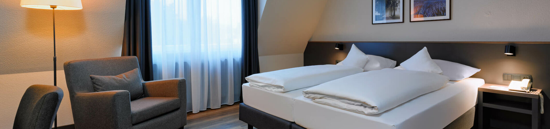 Superior Zimmer im ATLANTIC Hotel Landgut Horn Helles Hotelzimmer mit Doppelbett, Sessel, Lampe und Bildern an der Wand, ATLANTIC Hotel Landgut Horn Bremen.