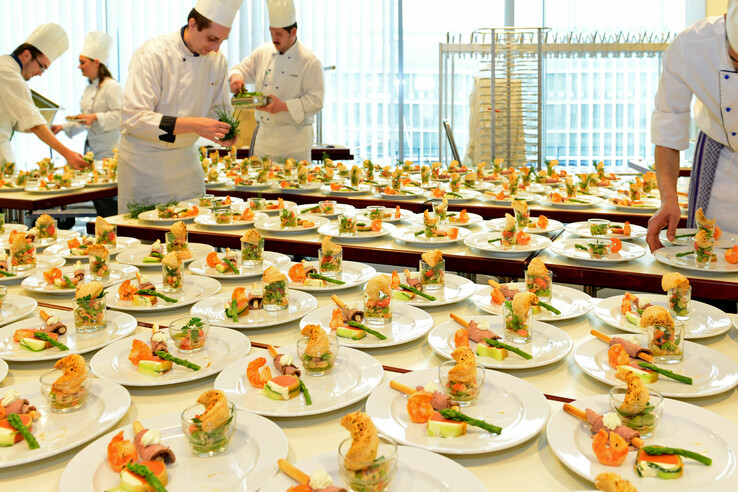 Köche richten zahlreiche Teller mit kunstvoll angerichteten Vorspeisen in einer Hotelküche an.