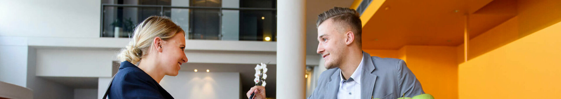Woman at the reception desk of the ATLANTIC Hotel Universum, Bremen, talking to a member of staff.