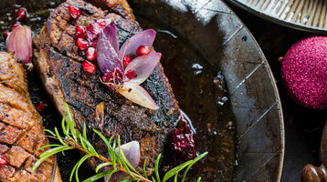 Gebratene Entenbrust in Pfanne mit Granatapfel, Rosmarin und Rotkohl, festlich dekoriert mit roten Kugeln.