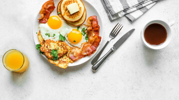 A breakfast plate with pancakes, bacon, fried eggs and potato hash browns, served with coffee and orange juice.