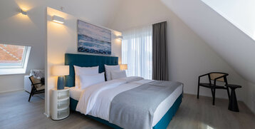 Modernes Hotelzimmer mit Doppelbett, stilvollen Möbeln, großem Fenster und Wandkunst im ATLANTIC Grand Hotel Travemünde.