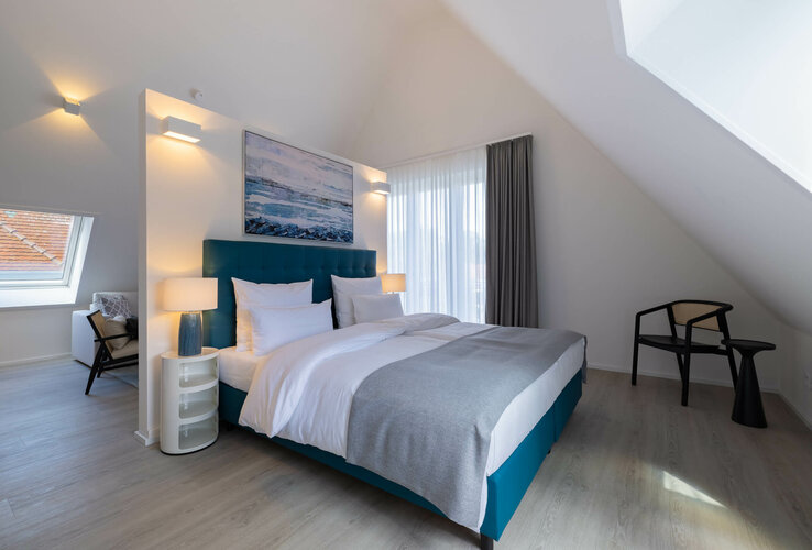 Modernes Hotelzimmer mit Doppelbett, stilvollen Möbeln, großem Fenster und Wandkunst im ATLANTIC Grand Hotel Travemünde.