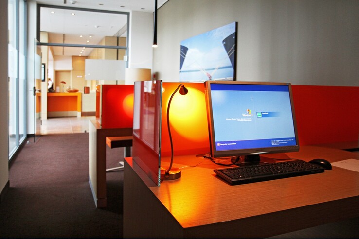Moderner Arbeitsbereich im ATLANTIC Hotel Kiel mit Computer, Schreibtisch und leuchtend roten Trennwänden.