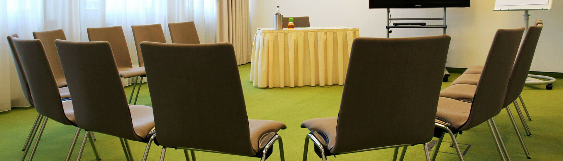 Konferenzraum im ATLANTIC Hotel Kiel mit Stuhlkreis, Flipchart und TV auf grünem Teppich.