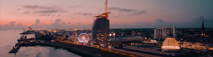 Abendliche Skyline von Bremerhaven mit ATLANTIC Hotel Sail City und beleuchtetem Riesenrad am Wasser.