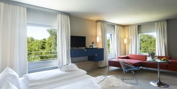 Modern hotel room with two beds, red sofa, large window and view of green trees in the ATLANTIC Hotel Universum.
