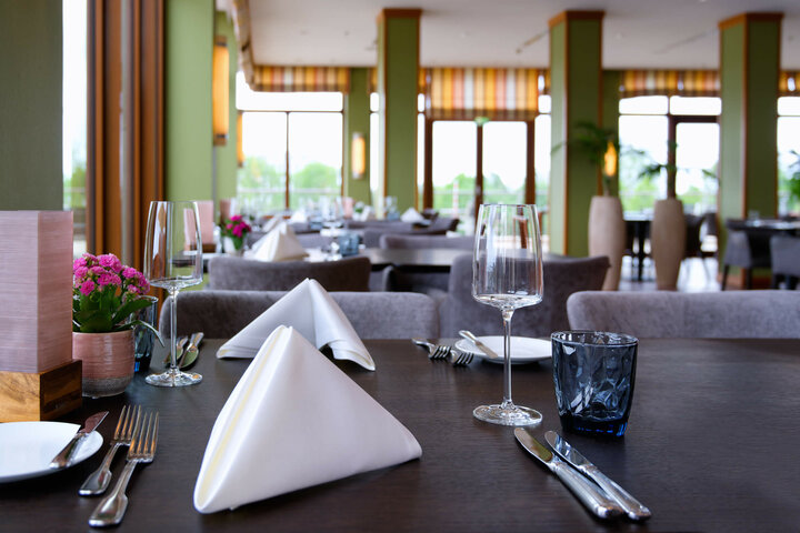 Restaurant Harbour View im ATLANTIC Hotel Wilhelmshaven Elegantes Hotelrestaurant mit gedeckten Tischen, weißen Servietten, Weingläsern und Blumenarrangements.