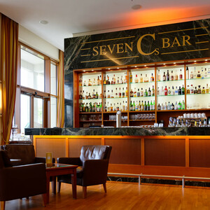 Seven Cs Bar im ATLANTIC Hotel Wilhelmshaven Elegante Hotelbar mit beleuchtetem Regal voller Spirituosen, gemütliche Ledersessel und Holzboden.