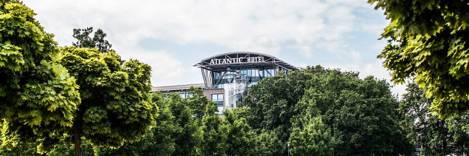ATLANTIC Hotel Airport in Bremen, surrounded by green trees and manicured lawns under a blue sky.