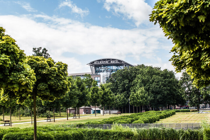 ATLANTIC Hotel Airport ATLANTIC Hotel Airport in Bremen, surrounded by green trees and manicured lawns under a blue sky.