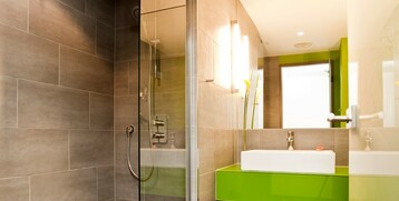 Modernes Badezimmer mit ebenerdiger Dusche, grüner Waschtisch und großer Spiegel im ATLANTIC Hotel Kiel.
