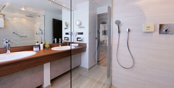 Modernes Badezimmer mit Doppelwaschbecken, großer Spiegelwand und ebenerdiger Dusche im ATLANTIC Hotel Landgut Horn.