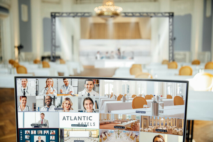 Konferenzraum im ATLANTIC Grand Hotel Travemünde mit Bildschirm für Videokonferenzen und elegant gedeckten Tischen.
