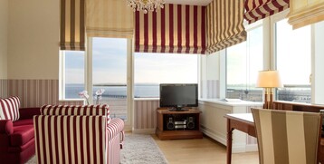 Bright hotel room with striped furniture, large window with sea view, desk, lamp and TV.