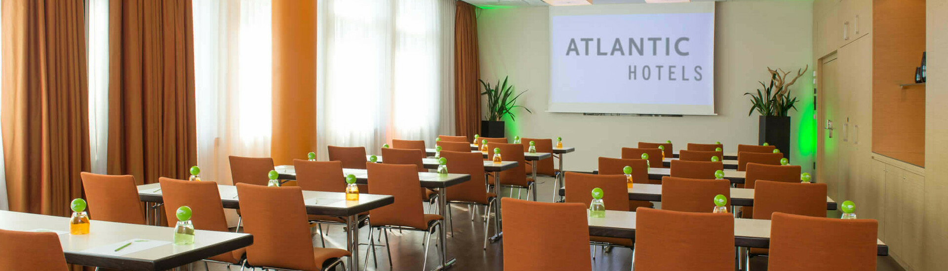 Moderner Konferenzraum im ATLANTIC Hotel Kiel mit Reihen von Tischen und Stühlen, Leinwand und natürlichem Licht.