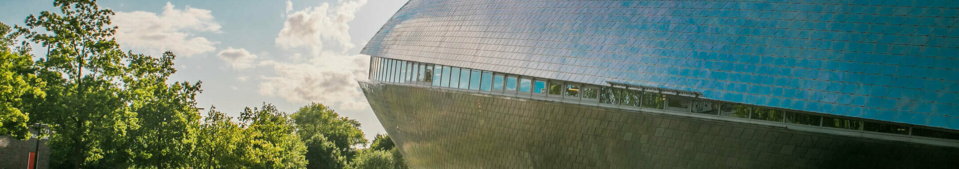 Futuristic building of Universum Bremen with reflective facade, surrounded by trees and water, in sunshine.