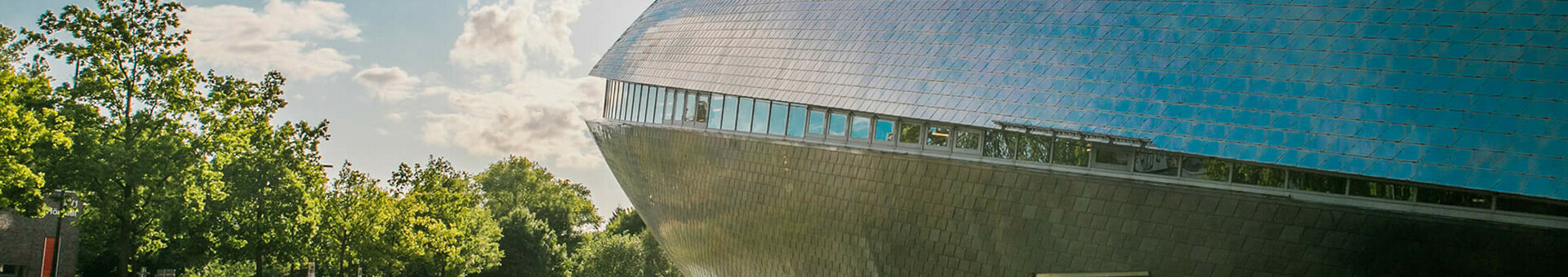Futuristisches Gebäude des Universum Bremen mit reflektierender Fassade, umgeben von Bäumen und Wasser, bei Sonnenschein.