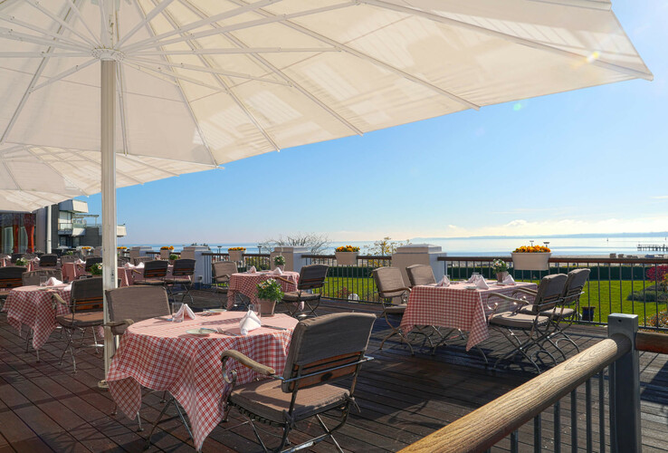 Terrasse des ATLANTIC Grand Hotel Travemünde mit gedeckten Tischen, Sonnenschirmen und Meerblick im Hintergrund.