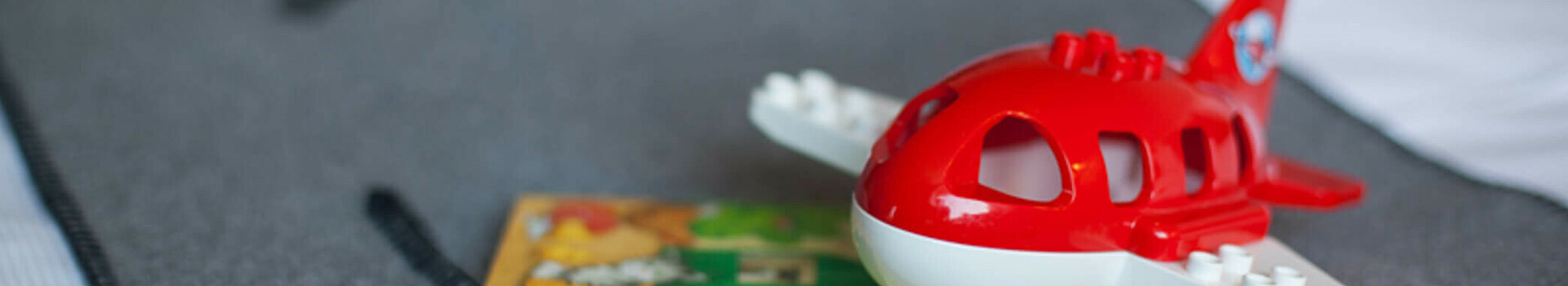 ATLANTIC Hotel Airport Bremen Familien Special Spielzeugflugzeug und Kinderbuch auf grauer Bettdecke im ATLANTIC Hotel Airport Bremen.