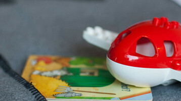 Toy airplane and children's book on a grey bedspread at the ATLANTIC Hotel Airport Bremen.