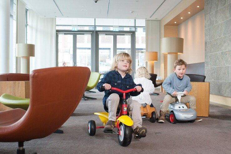 Kinder spielen auf Rutschfahrzeugen in der Lobby des ATLANTIC Hotels Kiel.