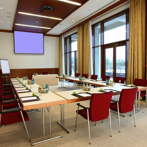 Conference room at the ATLANTIC Hotel Wilhelmshaven with a U-shaped table arrangement, red chairs and a view of a terrace.