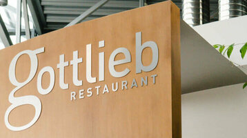 Modernes Restaurant mit Holzverkleidung, Glasdach und Pflanzen im Innenbereich.