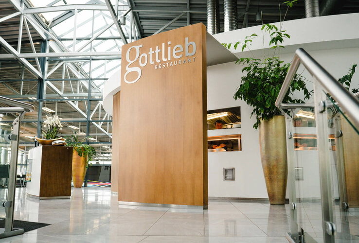 Modernes Restaurant mit Holzverkleidung, Glasdach und Pflanzen im Innenbereich.