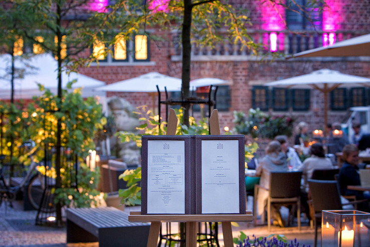 Menu on easel in the illuminated garden restaurant of the ATLANTIC Grand Hotel Bremen, guests in the background.
