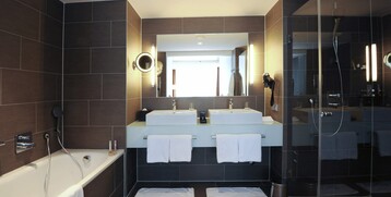 Modernes Hotelbad mit Badewanne, Doppelwaschbecken, großer Spiegel und Glasdusche im ATLANTIC Grand Hotel Bremen.
