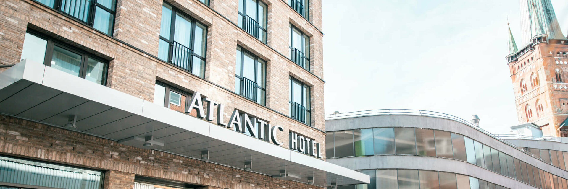 ATLANTIC Hotel Lübeck Hoteleingang Aussenansicht mit Kirche im Hintegrund