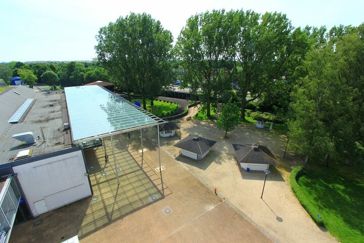 Luftaufnahme des ATLANTIC Hotel Galopprennbahn, umgeben von Bäumen und Grünflächen, mit überdachtem Eingangsbereich.
