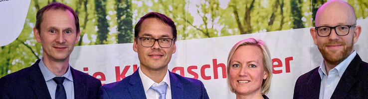 Pressemitteilung Klimaschutz Preisträger 2018 Vier Personen in Anzügen halten Auszeichnungen vor einem Banner mit "energie konsens"-Logo.