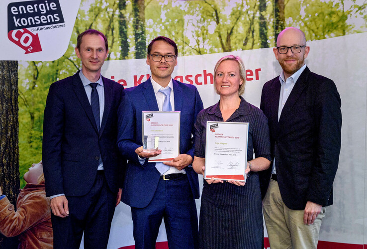 Pressemitteilung Klimaschutz Preisträger 2018 Four people in suits hold awards in front of a banner with the "energie konsens" logo.