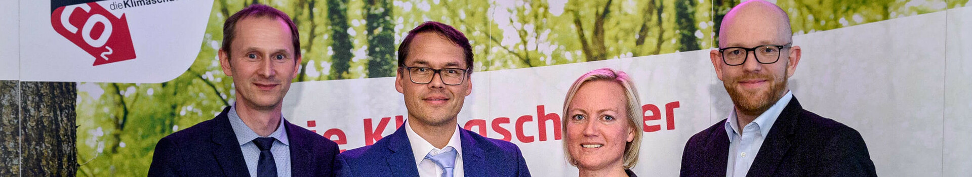 Vier Personen in Anzügen halten Auszeichnungen vor einem Banner mit "energie konsens"-Logo.