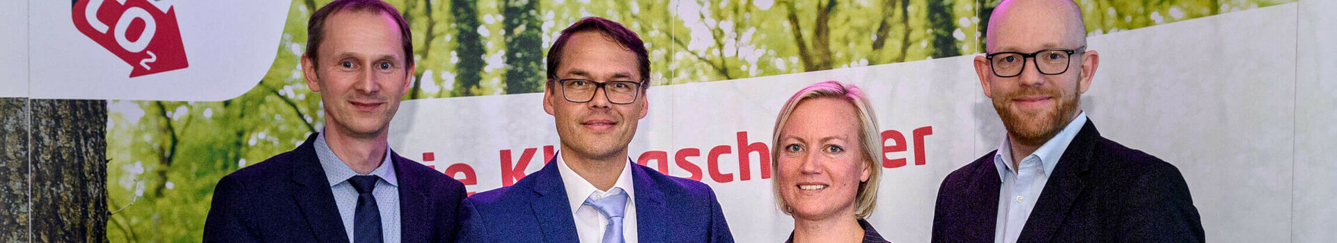 Four people in suits hold awards in front of a banner with the "energie konsens" logo.