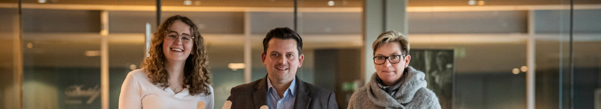 Three people in the ATLANTIC Hotel, holding a "Moin" sign and a tablet with "Future Sales Convention".