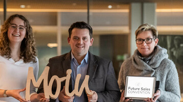 Ansprechpartner für den Messe- und Tagungsstandort Bremerhaven Drei Personen im ATLANTIC Hotel, halten ein "Moin"-Schild und ein Tablet mit "Future Sales Convention".