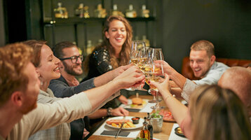 Eine Gruppe von Menschen stößt fröhlich mit Weingläsern an einem gedeckten Tisch an.